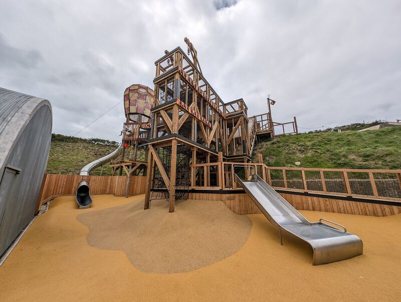 A large wooden fort playset with multiple decks, climbing wall, and twin slides
