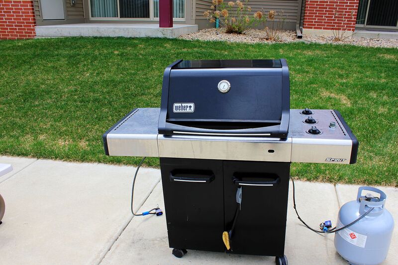 Weber Spirit gas grill on a residential driveway with propane tank attached