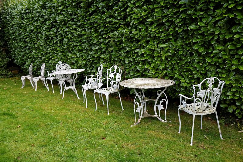 White wrought-iron patio table and chairs on a green lawn beside a hedge